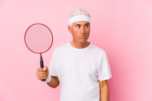 Middle aged man playing badminton isolated confused, feels doubtful and unsure.