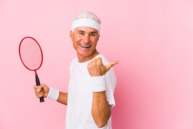 Middle aged man playing badminton isolated points with thumb finger away, laughing and carefree.
