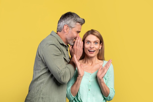 Middle aged man sharing secret or whispering gossips into his wife39s ear spouses sharing shocking news