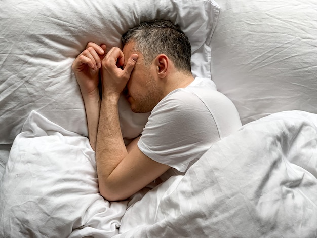 中年男性は自宅で眠っています 居心地の良い寝室のベッドは 白い振動で 独りで 朝早く 快適なコンセプト