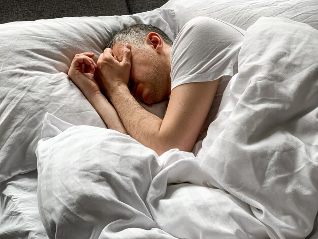 中年男性は自宅で眠っています 居心地の良い寝室のベッドは 白い振動で 独りで 朝早く 快適なコンセプト