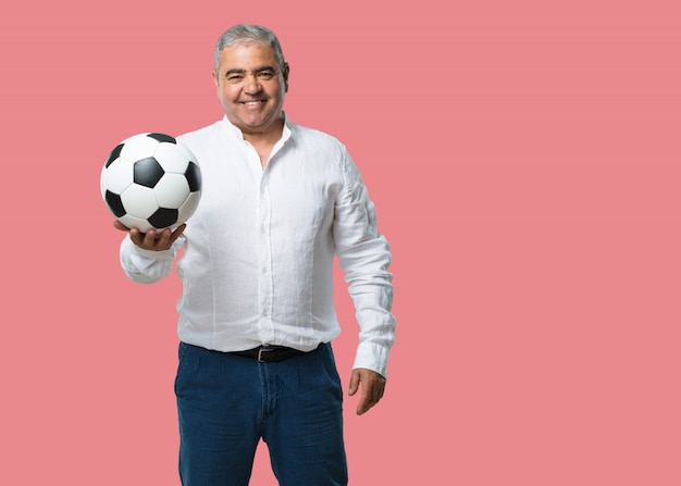 Middle aged man smiling and happy, holding a soccer ball, competitive attitude, excited to play a game