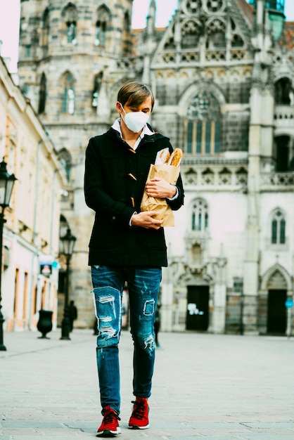 Uomo di mezza età per strada con pane, baguette, pagnotta durante la pandemia globale, indossando maschera, prendendo pane dal forno. cibo da asporto, spesa da forno durante il covid 19.