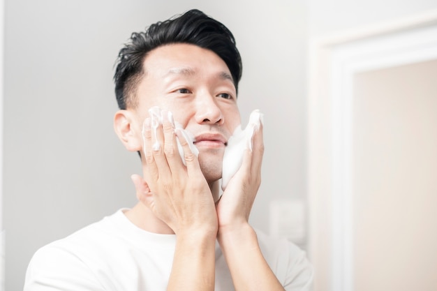 Middle-aged man washing his face with foam at wash basin