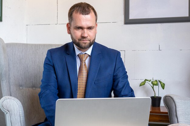 Uomo di mezza età con la barba in un vestito blu che usa un computer portatile in ufficio concetto di affari bel libero professionista maschio che lavora sul computer portatile sul posto di lavoro imprenditore digitando le informazioni