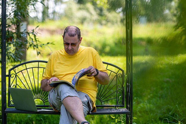 Middle aged man with laptop and documents working outside in garden green home office concept