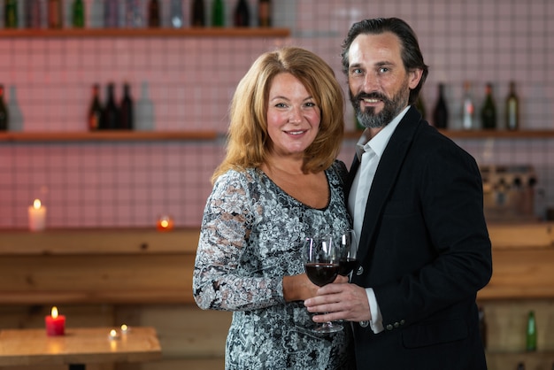 Middle-aged man and woman stand with raised glasses of wine and look into the camera
