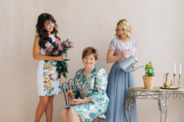 A middle-aged mother with two daughters, blonde with a watering can and a brunette with a bouquet of lilacs.