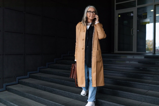 Middle aged older business woman talking on a mobile phone leaving the building concept of