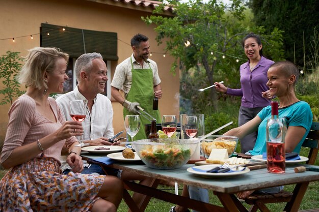 Фото Люди среднего возраста обедают и весело пьют красное вино вместе в домашнем саду