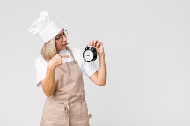 Middle-aged pretty baker woman holding an alarm clock