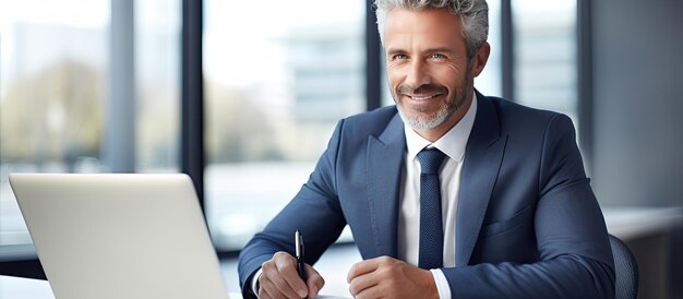 Middle aged professional sitting at desk in office working on laptop and taking notes