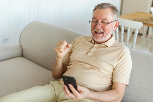 Middle aged senior man euphoric winner with smartphone older mature grandfather looking at cell phon