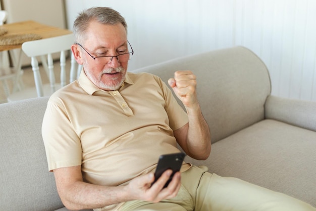 Middle aged senior man euphoric winner with smartphone older mature grandfather looking at cell phon