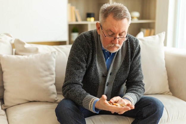 Middle aged senior man holding medical pills sitting on couch at home mature old senior grandfather