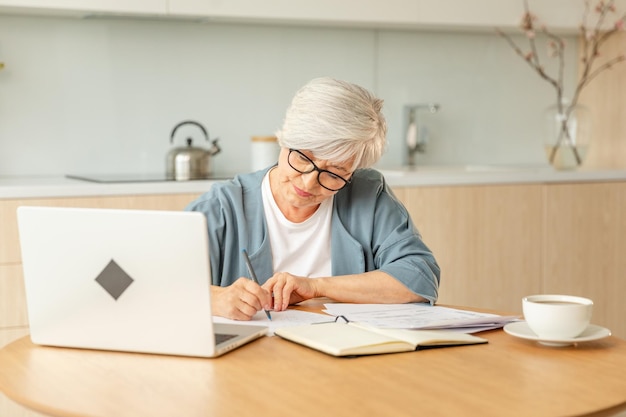 Photo middle aged senior woman using laptop computer writing notes at home focused mature old
