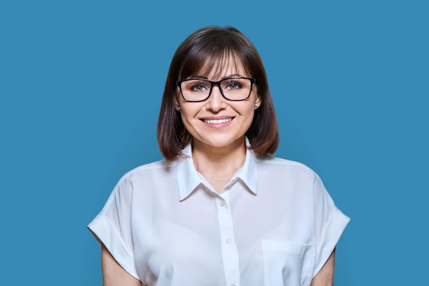 Middle aged smiling business woman over blue color background positive friendly 40s female looking at camera teacher psychologist profession psychology therapy success work staff concept