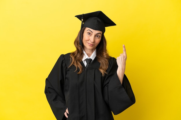 Middle aged university graduate isolated on yellow background showing and lifting a finger in sign of the best