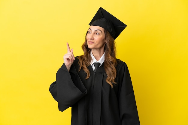 Middle aged university graduate isolated on yellow background thinking an idea pointing the finger up