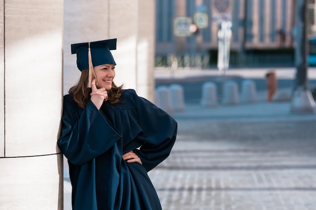 Middle aged woman in blue graduation gown and cap in campus\
with pillars