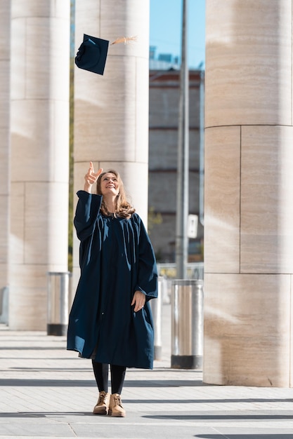 Middle aged woman in blue graduation gown throwing her cap in
campus with pillars
