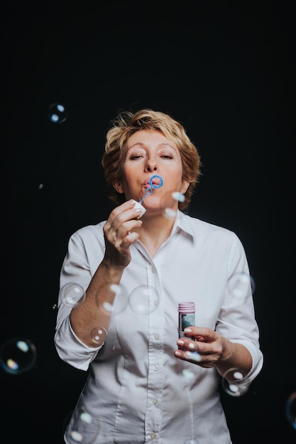 Photo middle aged woman in casual outfit blowing soap bubbles isolated on black