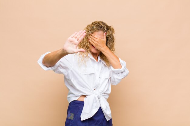 Photo middle aged woman covering face with hand and putting other hand up front to stop front, refusing photos or pictures