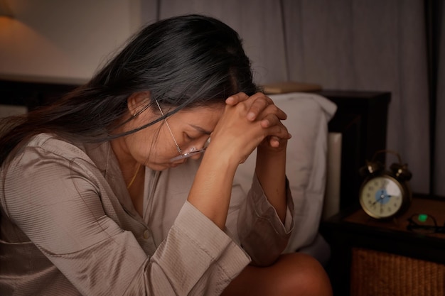 Middle aged woman depressed and stressed sitting beside the bed from insomnia