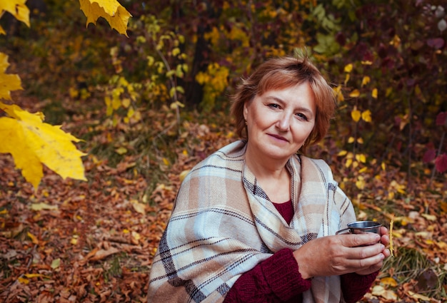 Middle-aged woman drinks tea in autumn forest