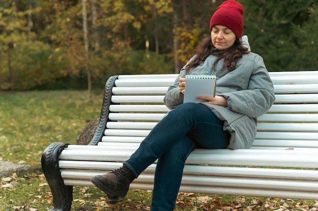 Middle aged woman enjoying the calm atmosphere of the park sitting on a bench creating wonderful sketches in her notebook