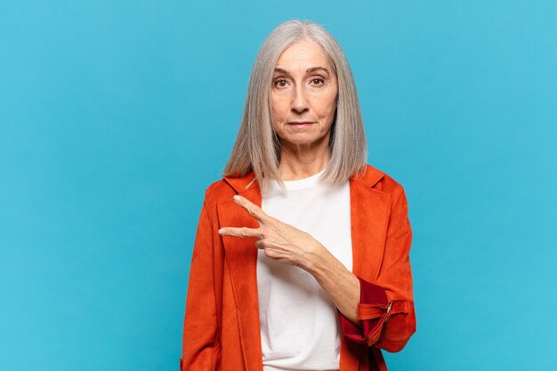 Middle aged woman feeling happy, positive and successful, with hand making v shape over chest, showing victory or peace