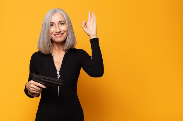 Middle aged woman feeling happy, relaxed and satisfied, showing approval with okay gesture, smiling