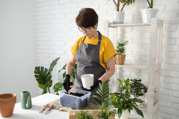 Pianta di trapianto di giardiniere donna di mezza età in vasi di ceramica sul concetto di tavolo in legno bianco di