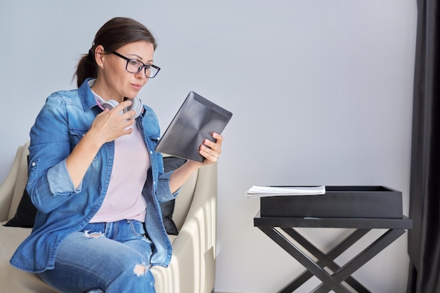 Photo middle aged woman in headphones with digital tablet at home on armchair