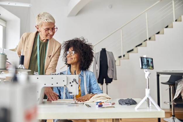 Photo middle aged woman helps young africanamerican colleague to sew in fashion studio