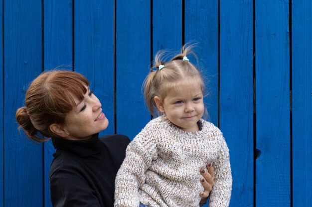 Middle aged woman holding child on hands on blue wooden background