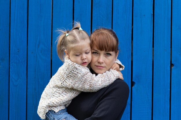 青い木製の背景に手で子供を保持している中年の女性