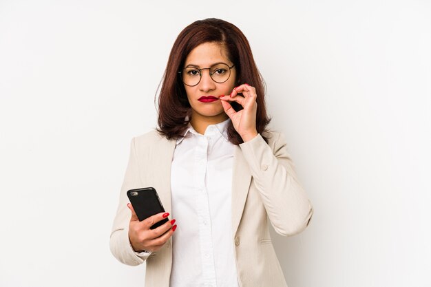 Middle aged woman holding a mobile phone with fingers on lips keeping a secret