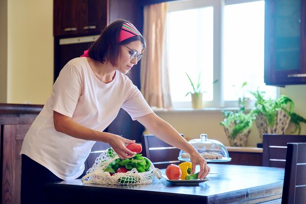 メッシュ繊維のエコバッグに新鮮な野菜を入れてキッチンで自宅で中年女性