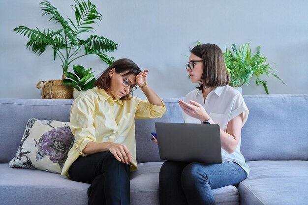 Middle aged woman in individual therapy female psychologist and patient sitting together on couch in office Psychology counseling psychotherapy mental health health care mature people concept