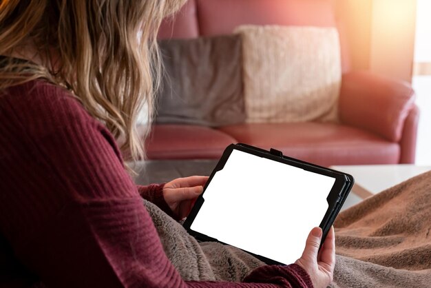 A middle-aged woman is lying on the couch at home she looks at tablet copy space