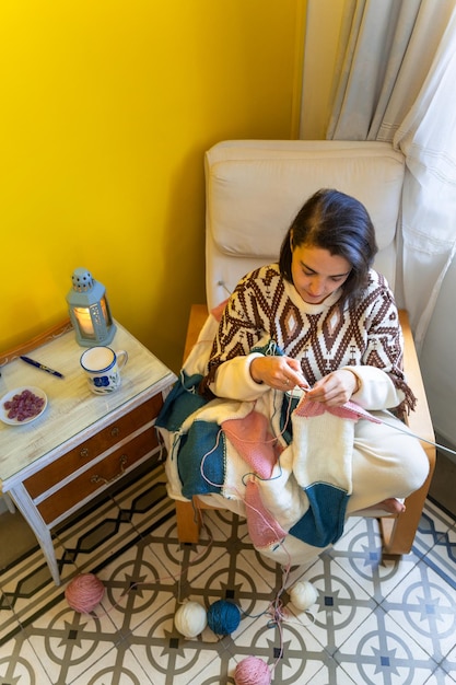 中年女性が床に羊毛のボールをつけて現代的な家で編み物をしています