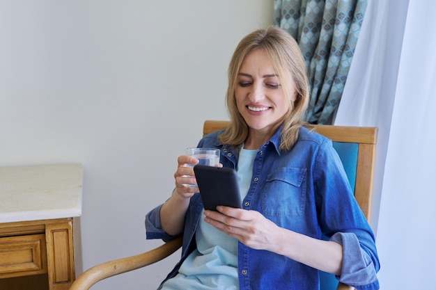 Middle aged woman looking at smartphone screen smiling talking