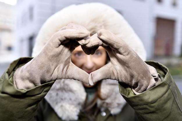 Foto donna di mezza età che fa un cuore con le mani per strada in inverno