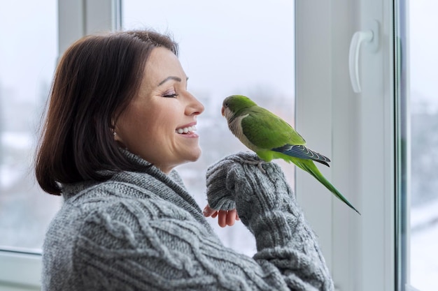 Middle aged woman and parrot together female bird owner talking looking at green quaker pet