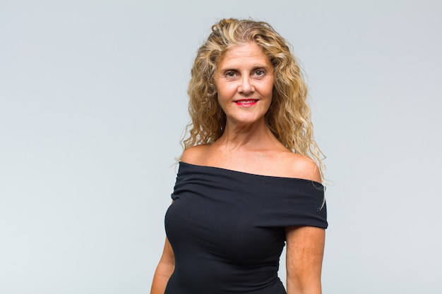 Middle aged woman posing and looking to front against white wall