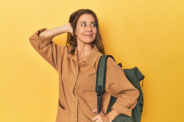 Photo middle aged woman prepped for hiking yellow studio shot touching back of head thinking