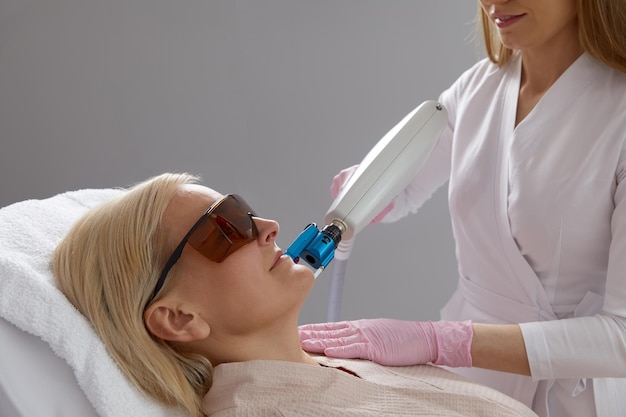 Middle aged Woman receiving laser treatment in cosmetology clinic wearing protective glasses