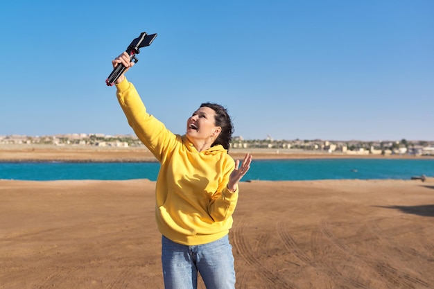 Middle aged woman recording video on smartphone sea vacation nature seascape background