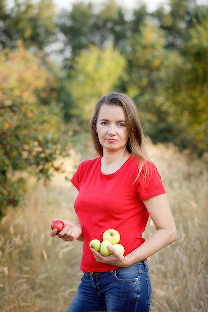 Middle aged woman in red t-shirt holding green apples in the garden